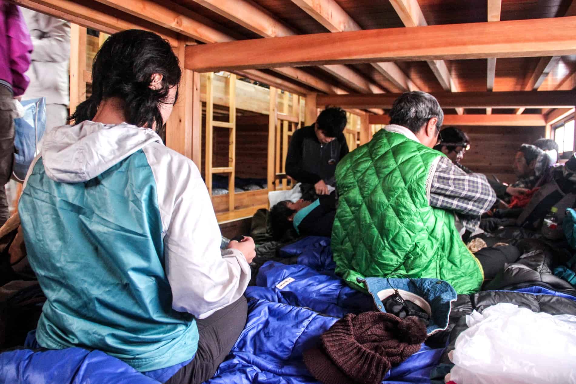 Japanese hikers on blue sleeping bags in a communal mountain hut on Mt. Fuji preparing their belongings. 