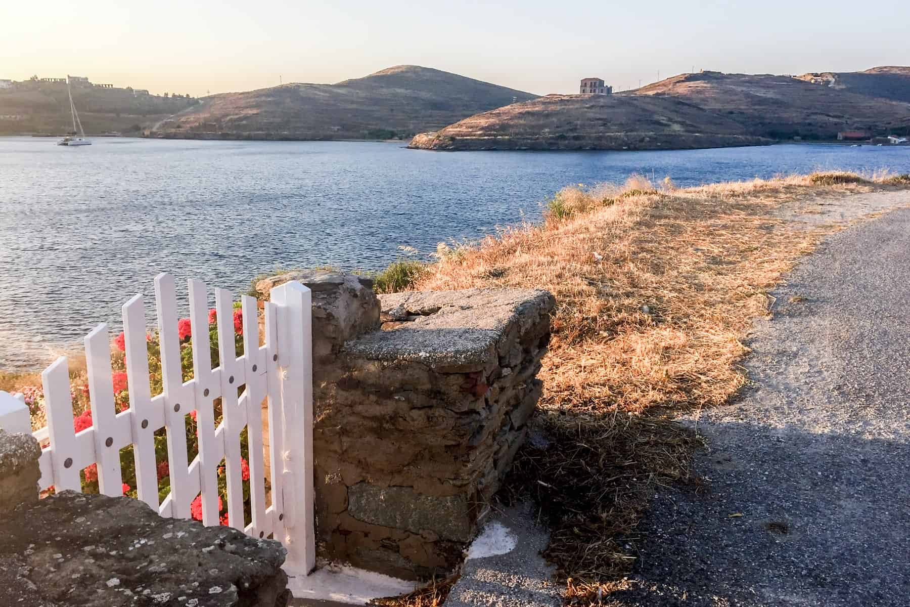 A walking trail curves around a coastline and the colour is of the sunset. A white picket fence gate looks as if it will open out to the sea behind it.