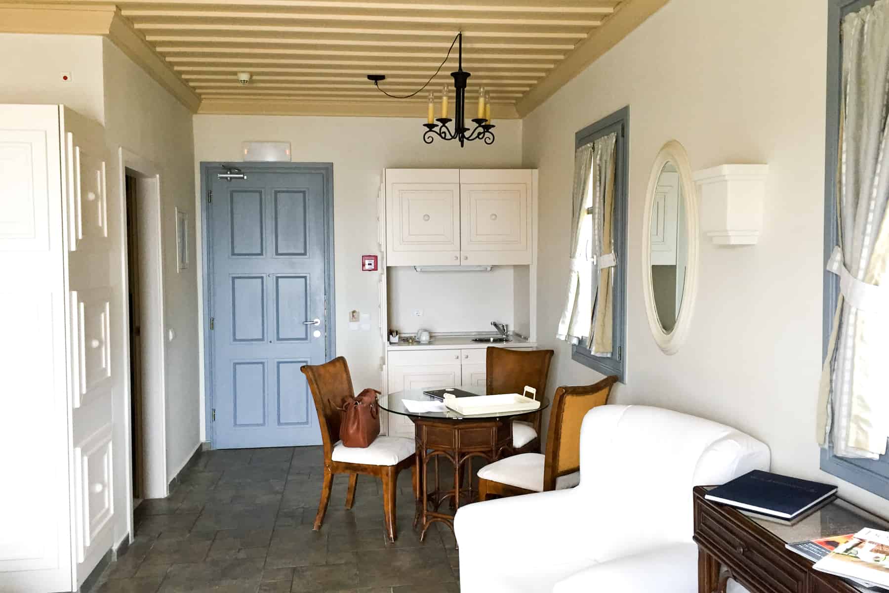 A modern hotel interior with an grey blue door, dark wooden table and white sofa at the Porto Kea suites in Greece