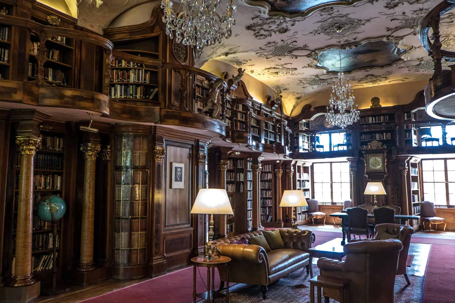 An old, classic, dark wood panelled interior of the library at Inside the library of Schloss Leopoldskron in Salzburg, Austria. The room is complete with a dark red carpet and leather sofas. 
