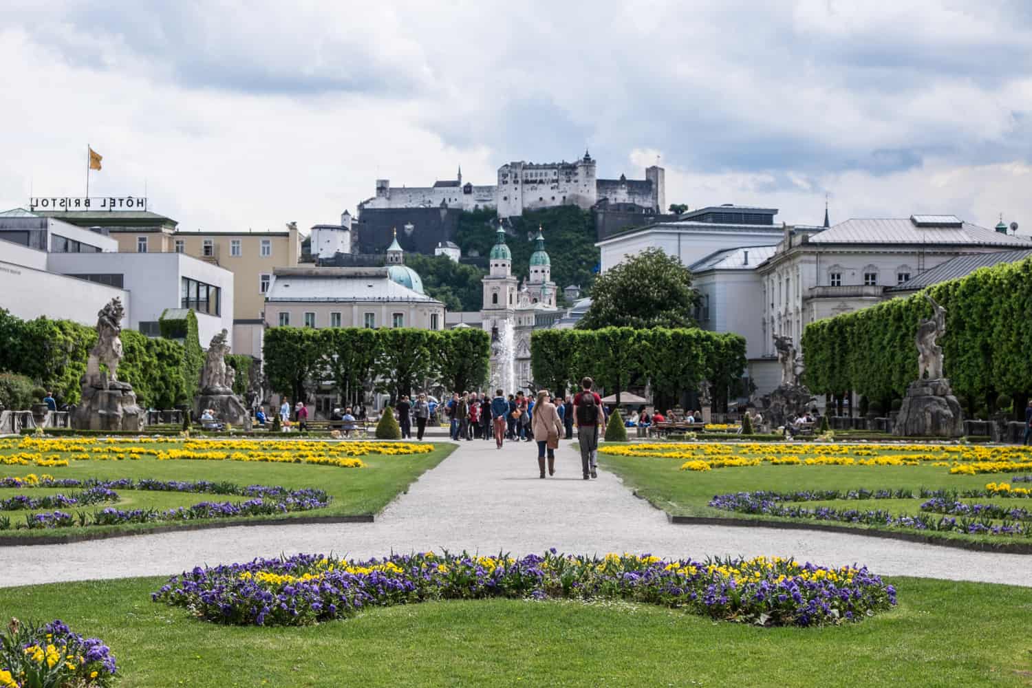 People walk through the manicured gras and flower beds of the Mirabell Gardens in Salzburg, which has a view towards towards the fortress on the hill. 