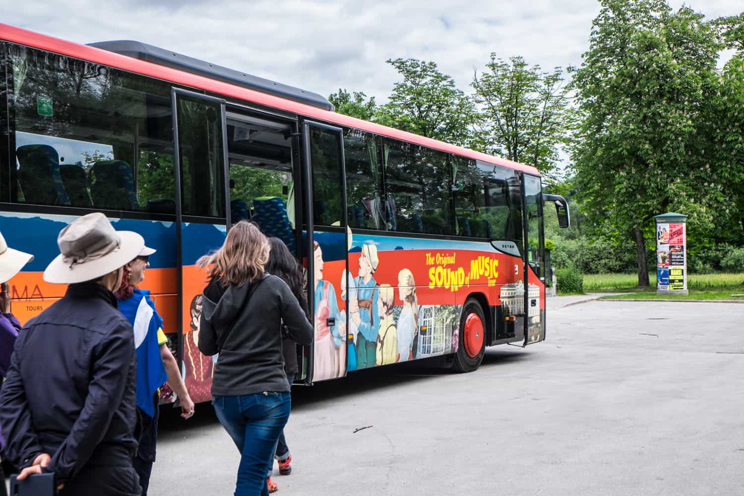 People walking towards a red and blue tour bus decorated with images of the characters from the Sound of Music. 