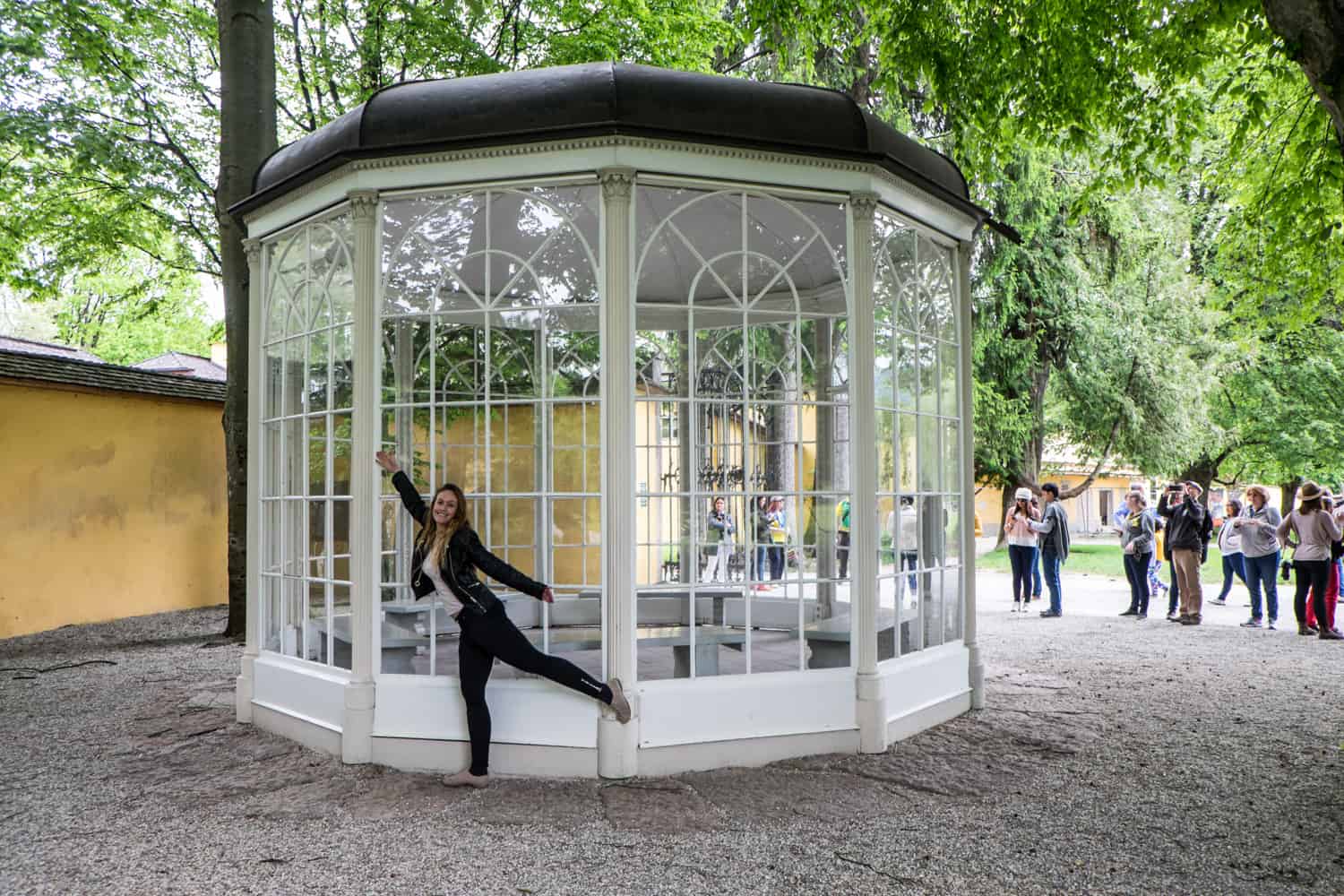 A woman dressed in black poses in a dance style outside a white and glass gazebo in Salzburg made famous in the Sound of Music. 
