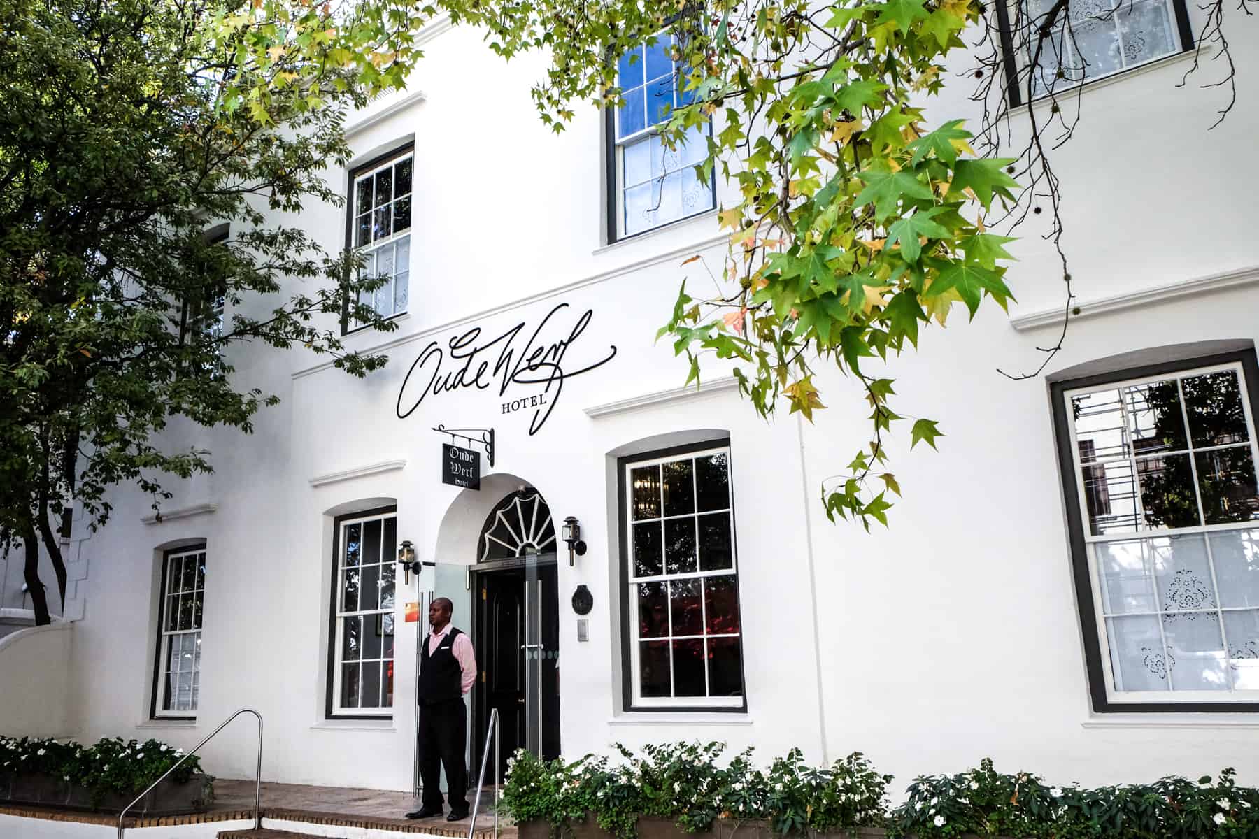 A man stands outside the white painted and planted covered Oude Werf hotel in Stellenbosch, South Africa