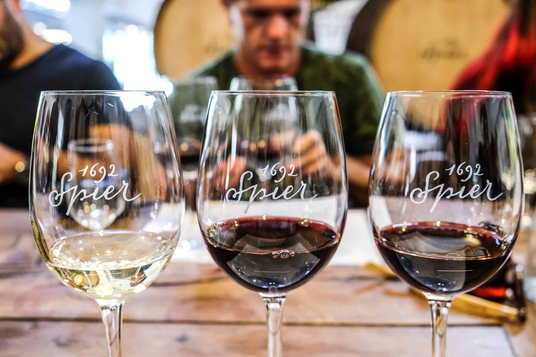 Three wine glasses, one containing white wine and two with red wine are lined up in a row as part of a wine tasting session. On the wine glasses is written 1692 Spier - the name of the vineyard in Stellenbosch, South Africa