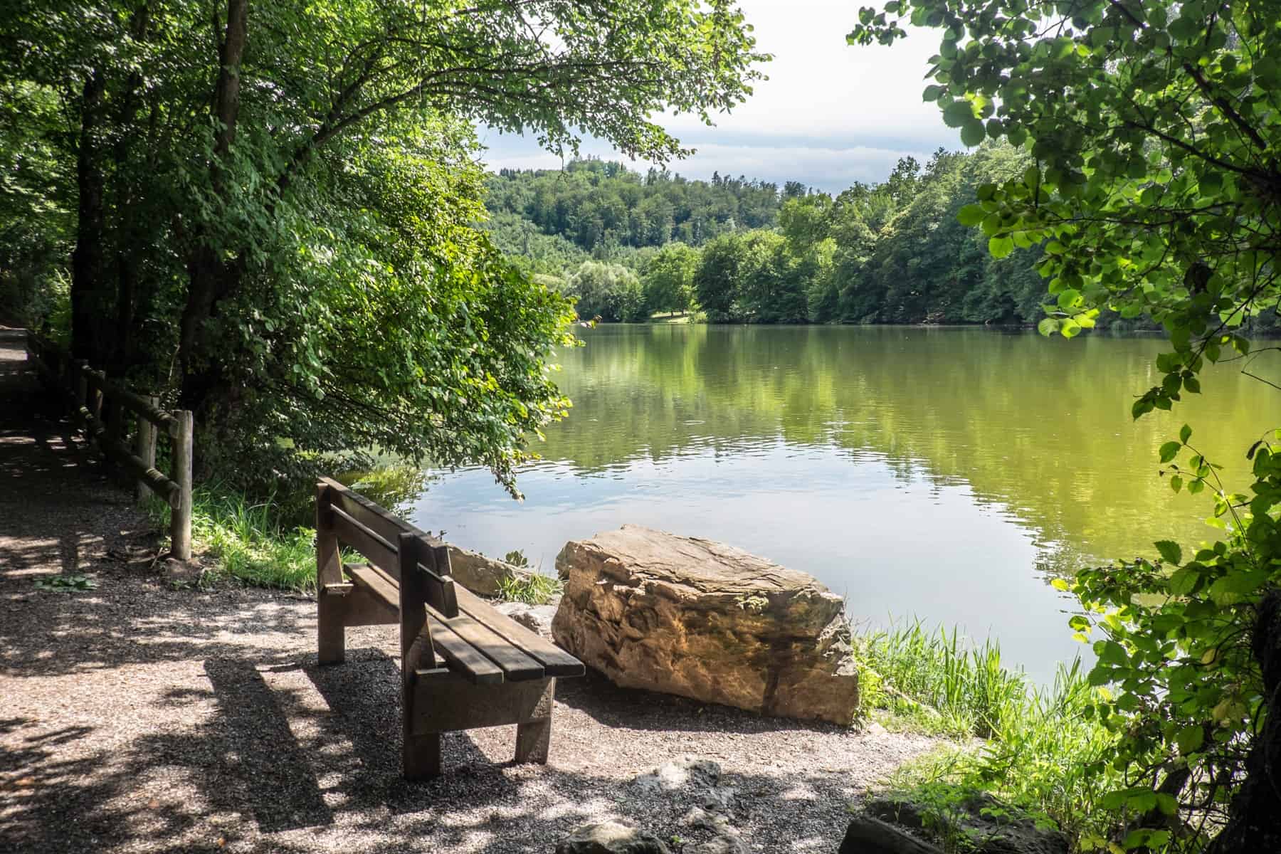 A bench next to the green tree-lined water of Thalersee Lake near Graz, Austria