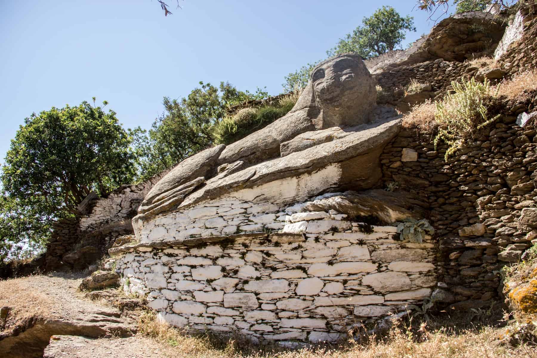 A stone lion sculpture on Kea Island known as Liontas, that sits in the wilderness on a tree lined trail 