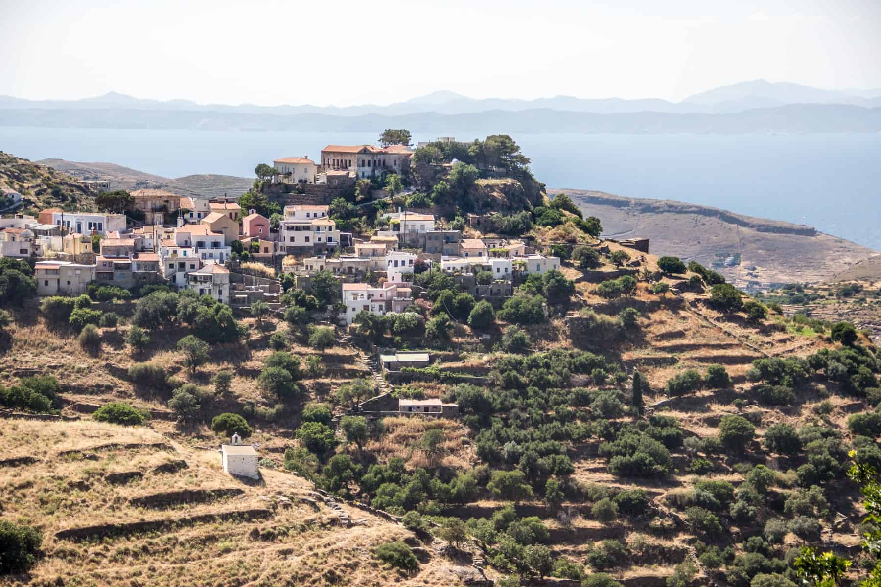 A pink and white village in Tzia Island Cyclades entirely surrounded by yellow terraced slopes