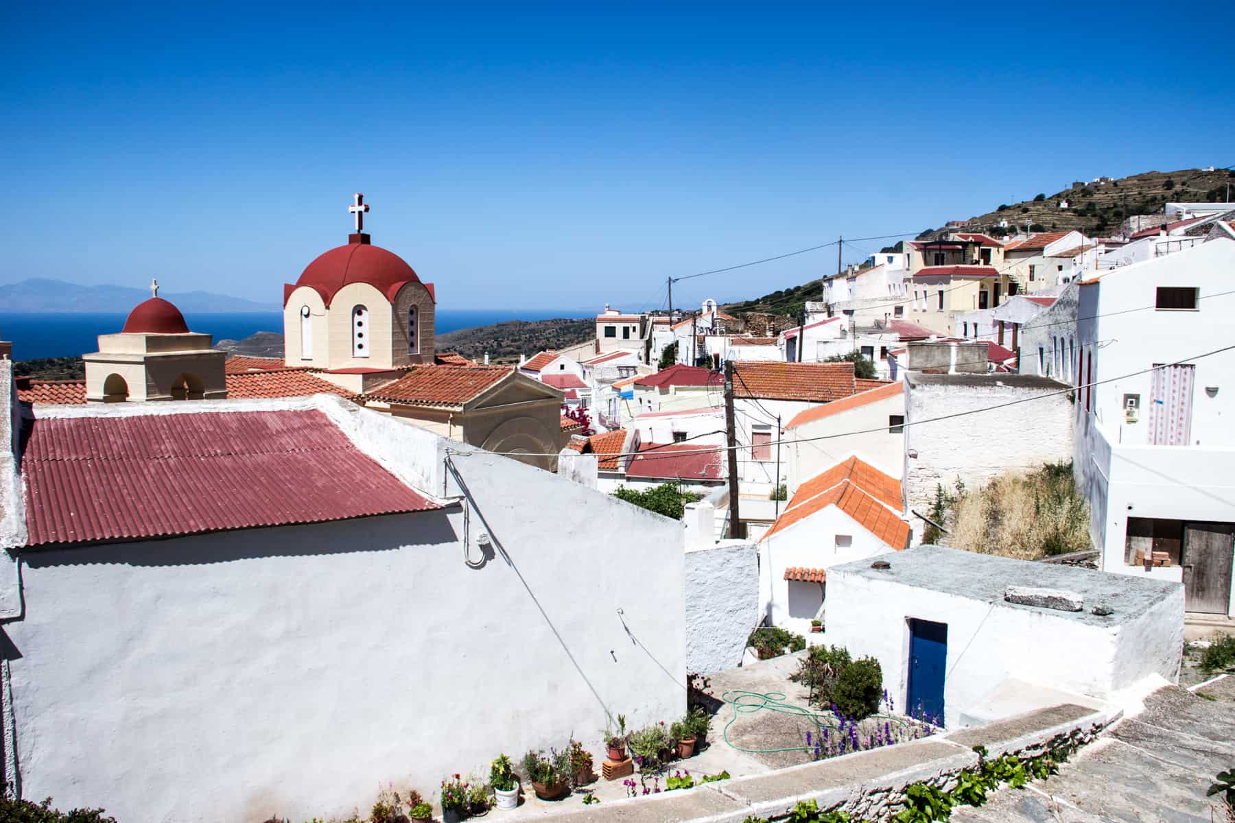 A blend of white houses with red rooftops, and a red spired church in the background - a far view of Ioulida town on Kea Island in Greece