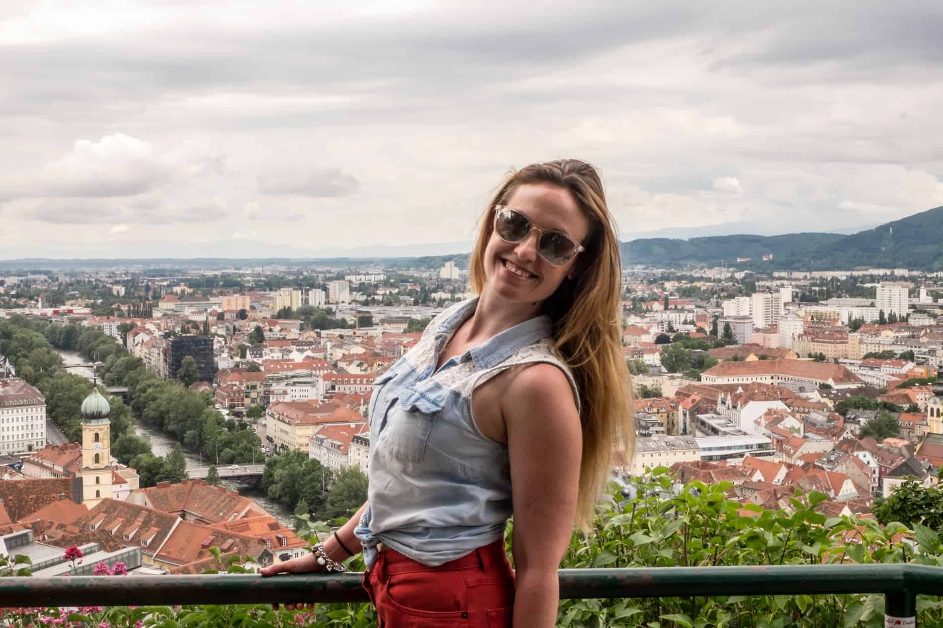 A woman smiles to camera to backdrop of Graz from the elevated viewpoint of the Schlossberg.