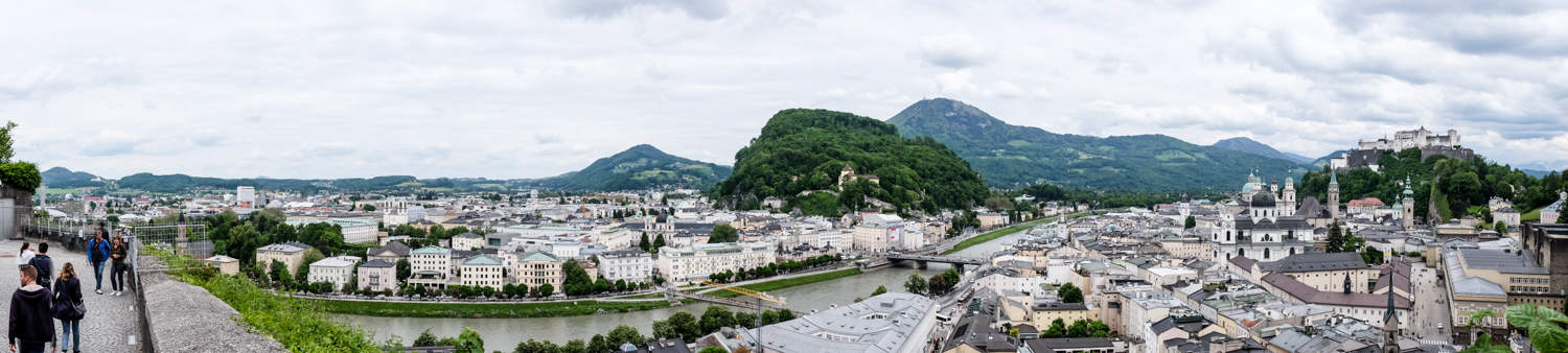 A panoramic view of Salzburg in Austria, with a scattering of white buildings cut in half by a river and backed by low mountains, as seen from the top of the Modern Art Museum.