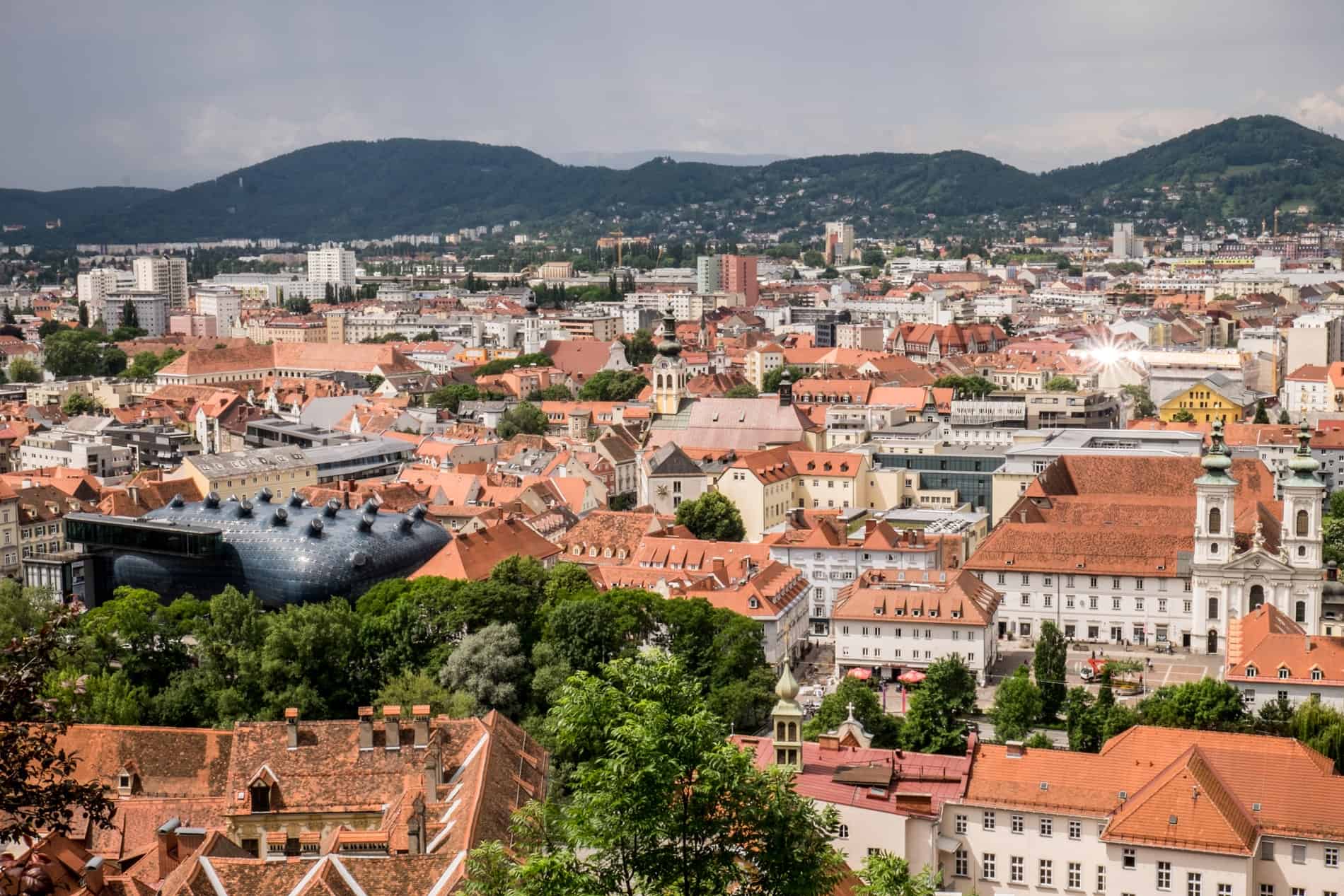 Elevated view of Graz city overlooking the red rooftops and the blue alien looking museum building.