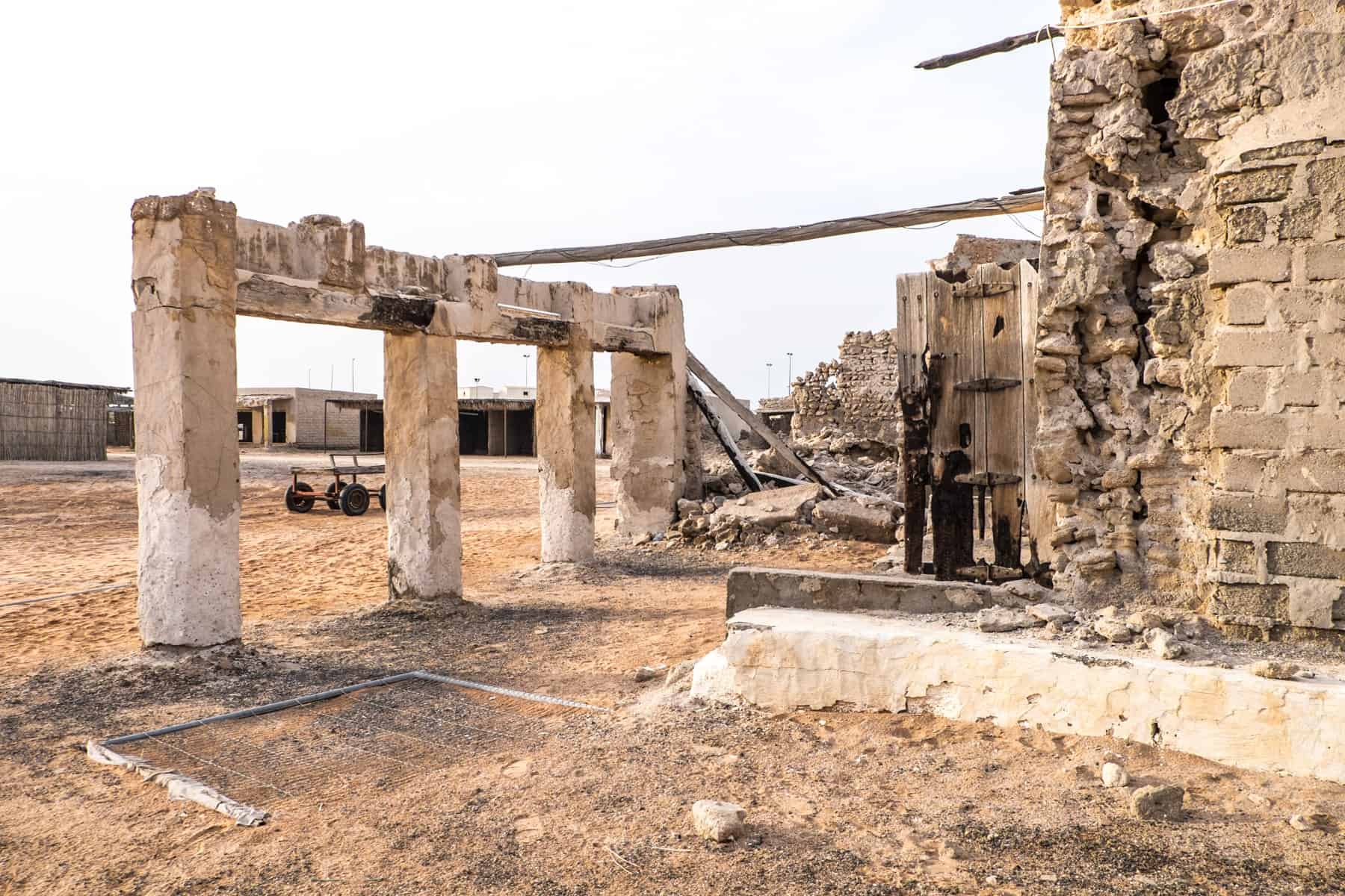 Four pillars of an old building wall stand next to a crumbling wall, connected by a single roof pole. Part of a ghost town in Ras Al Khaimah left over 60 years ago. 