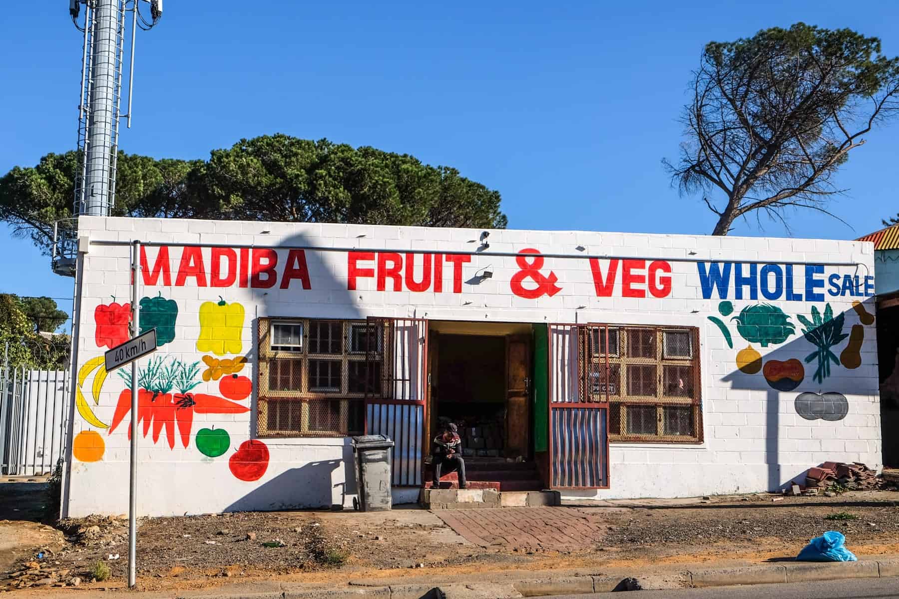A low block white building with red painted letters reading 'Madiba Fruit & Veg' in the kayamandi South Africa Township