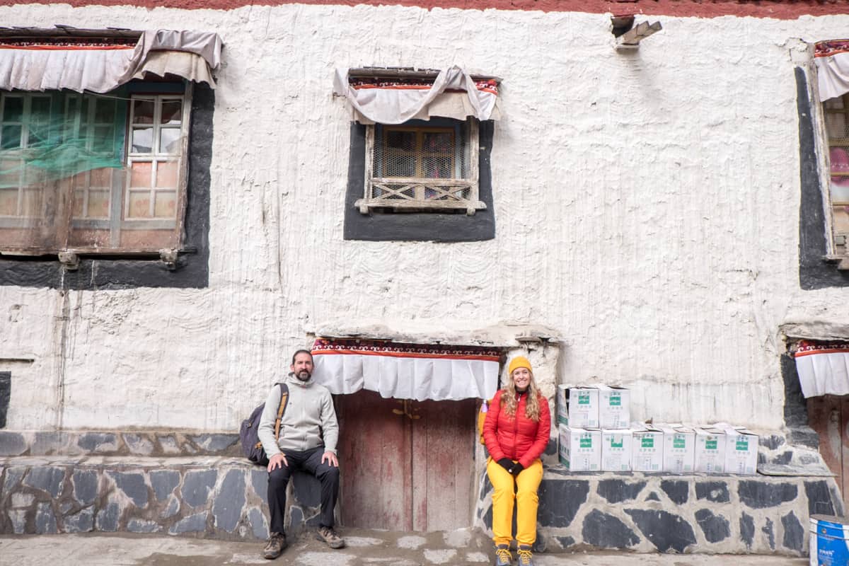A man in dark clothing and woman in red and yellow sit either side of a small doorway at a traditional Tibetan house in Gyantse when travelling in Tibet