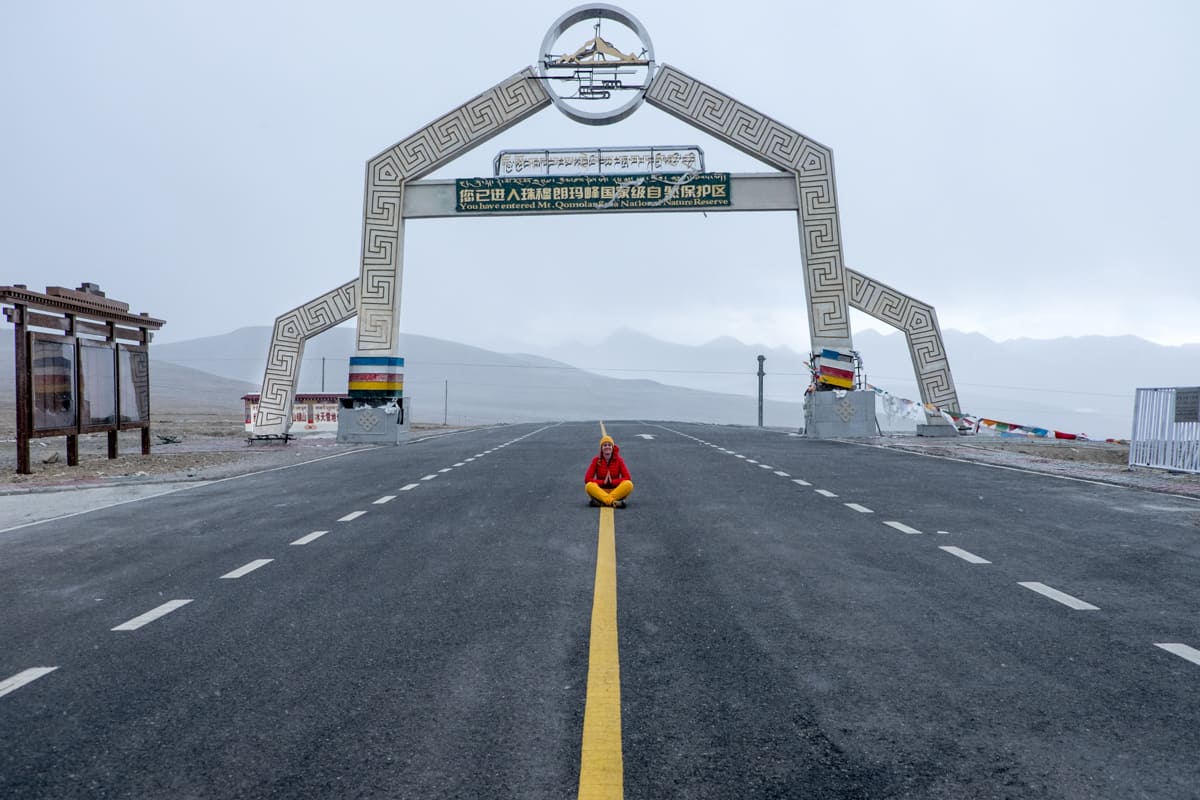 A female tourist dressed in red and orange sits in the road on the famous Gyatso Pass, the highest road in Tibet