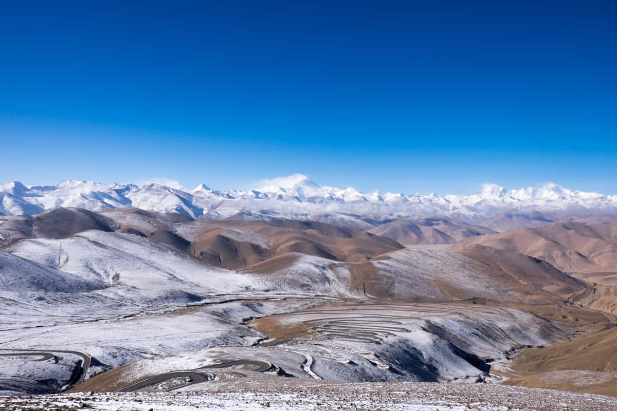 Panoramic views of the snow-capped brown, swirling Himalayan mountain range seen from a high road in Tibet