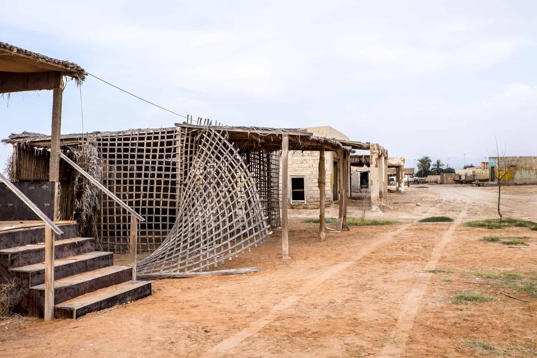 A wooden slat panel falls off the frame of a low building, abandoned in the orange earth of what was once the village of Al Jazirat Al Hamra in Ras Al Khaimah 