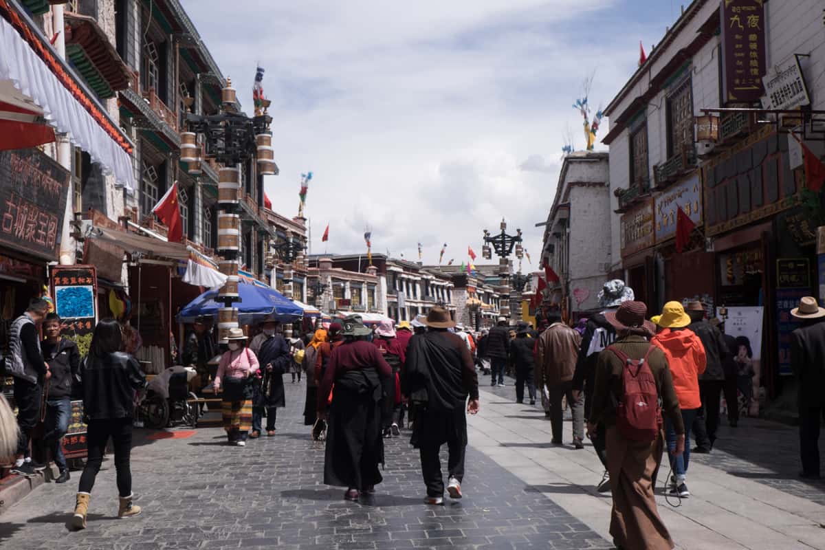 Tibetans on a pilgrimage walking the circular sacred Kora path in Lhasa lined by traditional white and flat-roofed buildings, experienced when you travel Tibet
