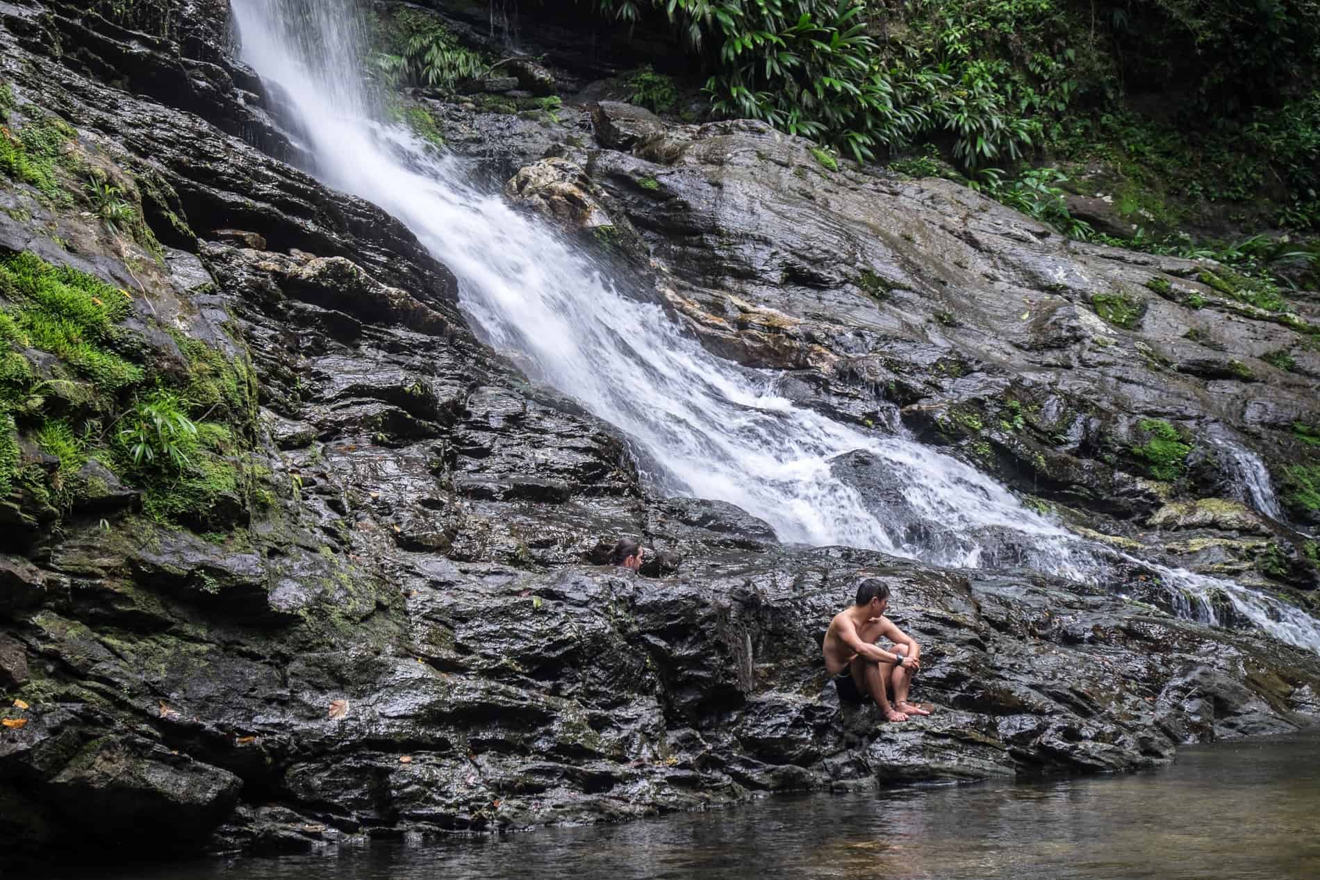 A man sitting on the rocks of a waterfall on the Lost City Trek.