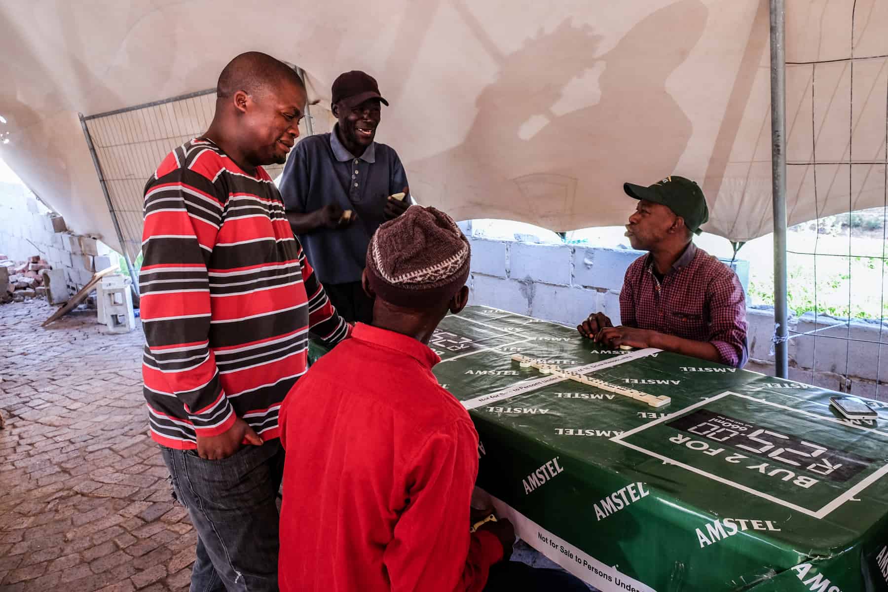 Four men play a game with white dominos on a table covered with a green cloth 