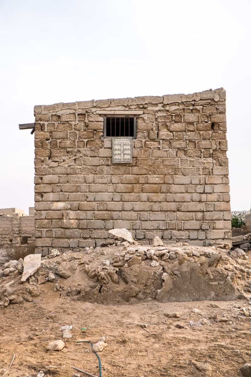 A rectangular, sandy beige brick structure, with one small window, crumbling and abandoned in the ghost town Al Jazirat Al Hamra in Ras Al Khaimah 