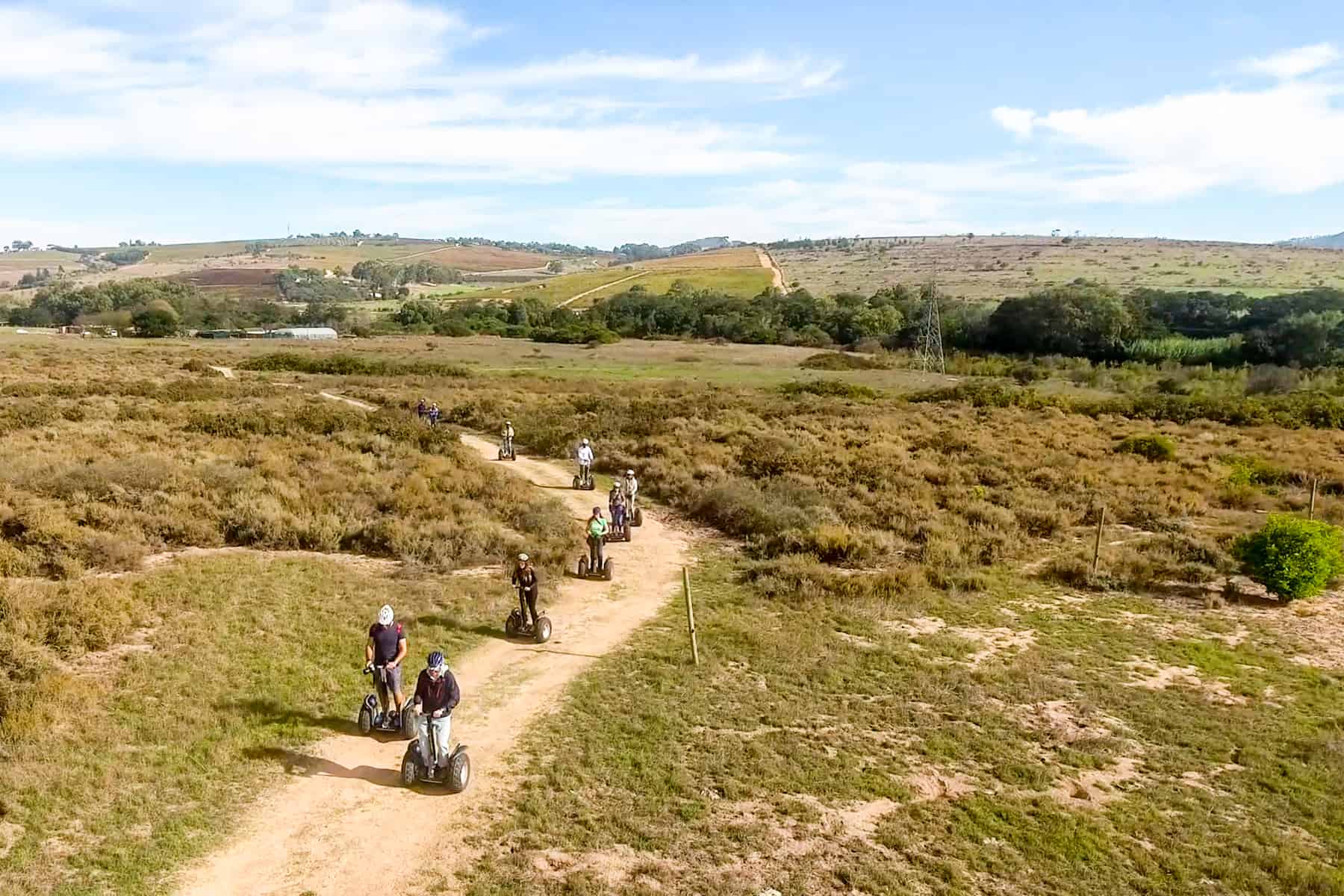 A group of people segway on a yellow path through a dusty green vineyard in Stellenbosch, South Africa