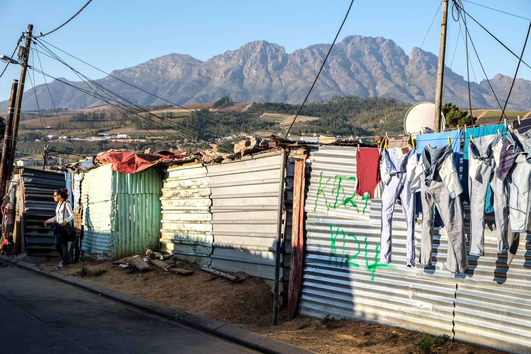 A row of single floor shanty houses in a Township in South Africa made of corrugated iron, painted green and white. Washing is hanging out to dry on the house on the left.