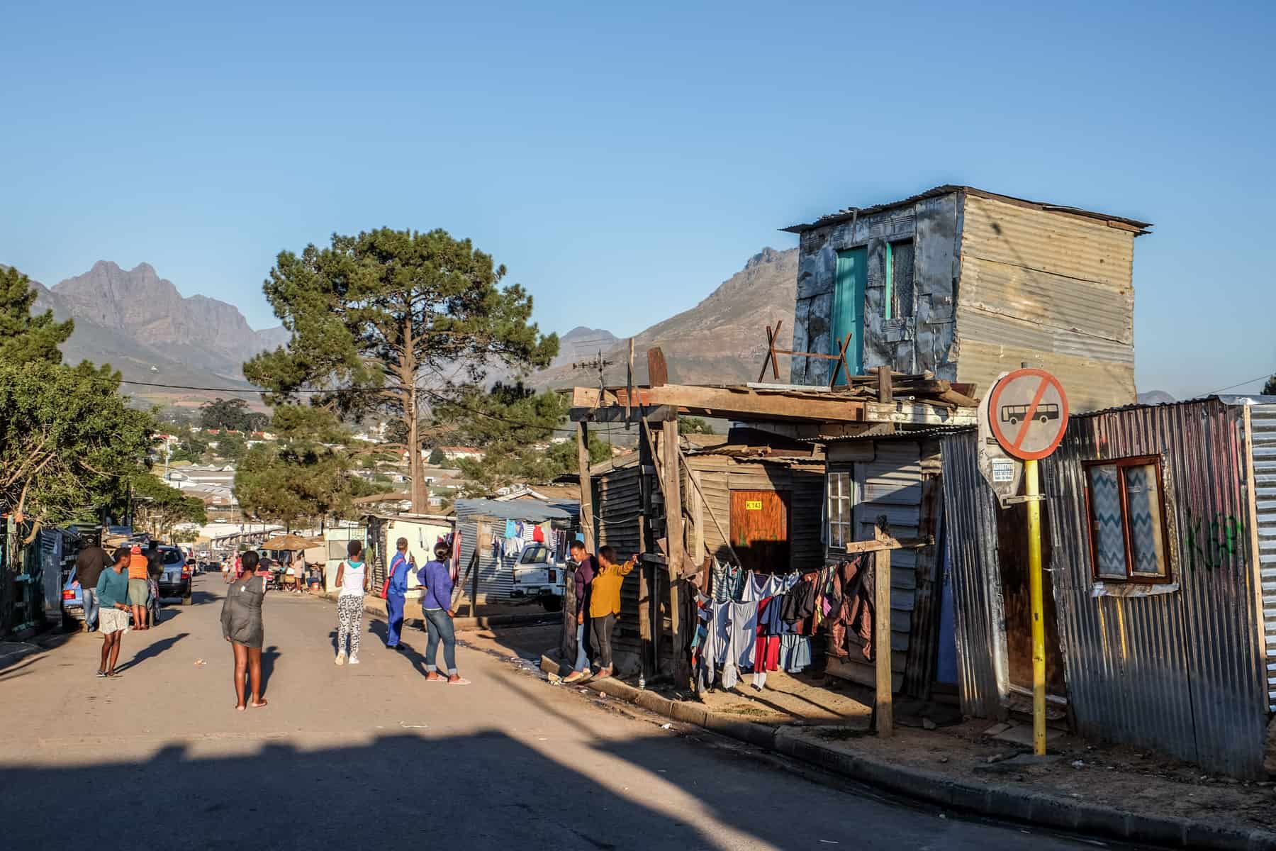 People on the streets next to shanty houses of the Kayamandi township in South Africa with mountains in the background