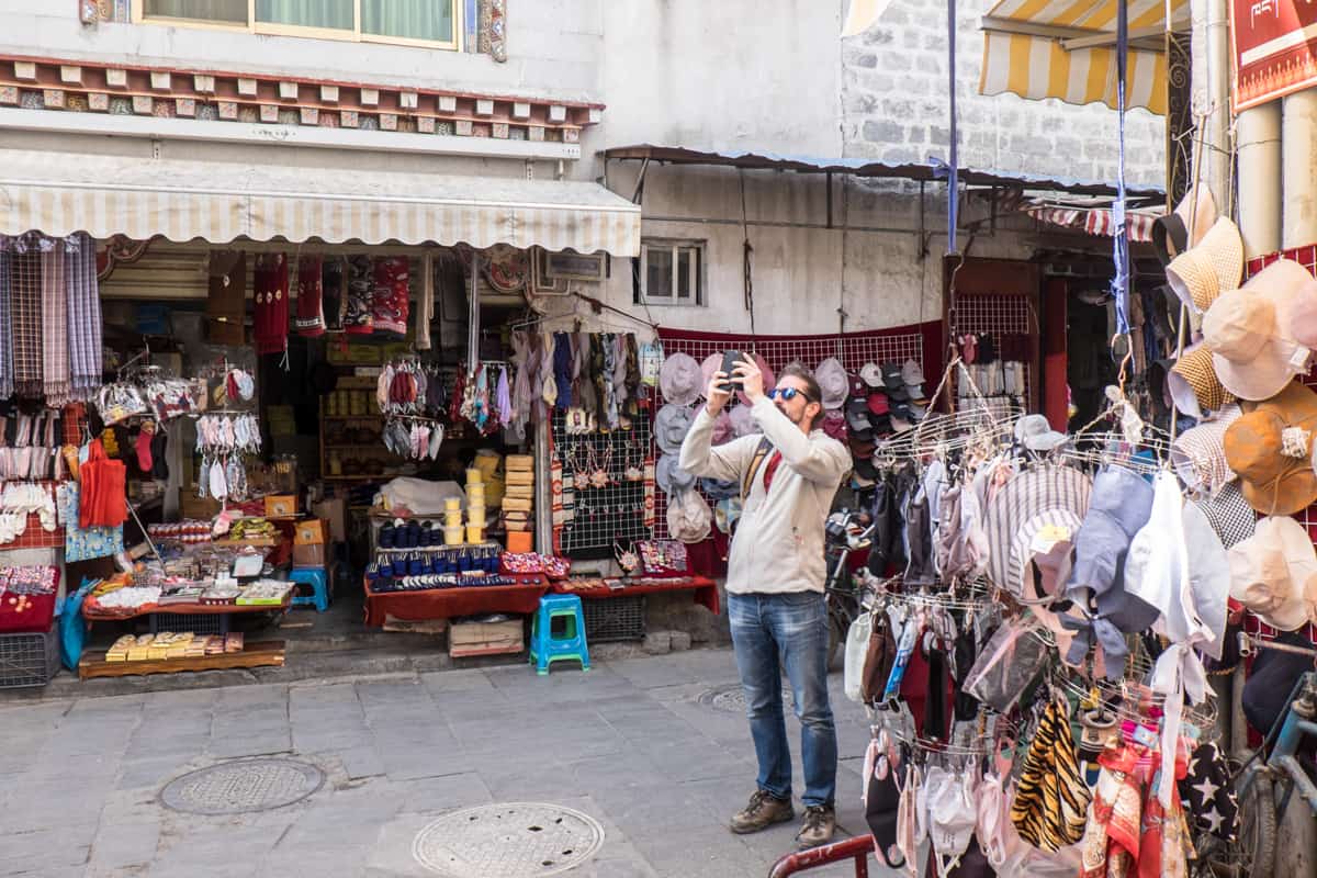 Male tourist taking a photo with his mobile phone on the shopping streets of Lhasa during Tibet travel