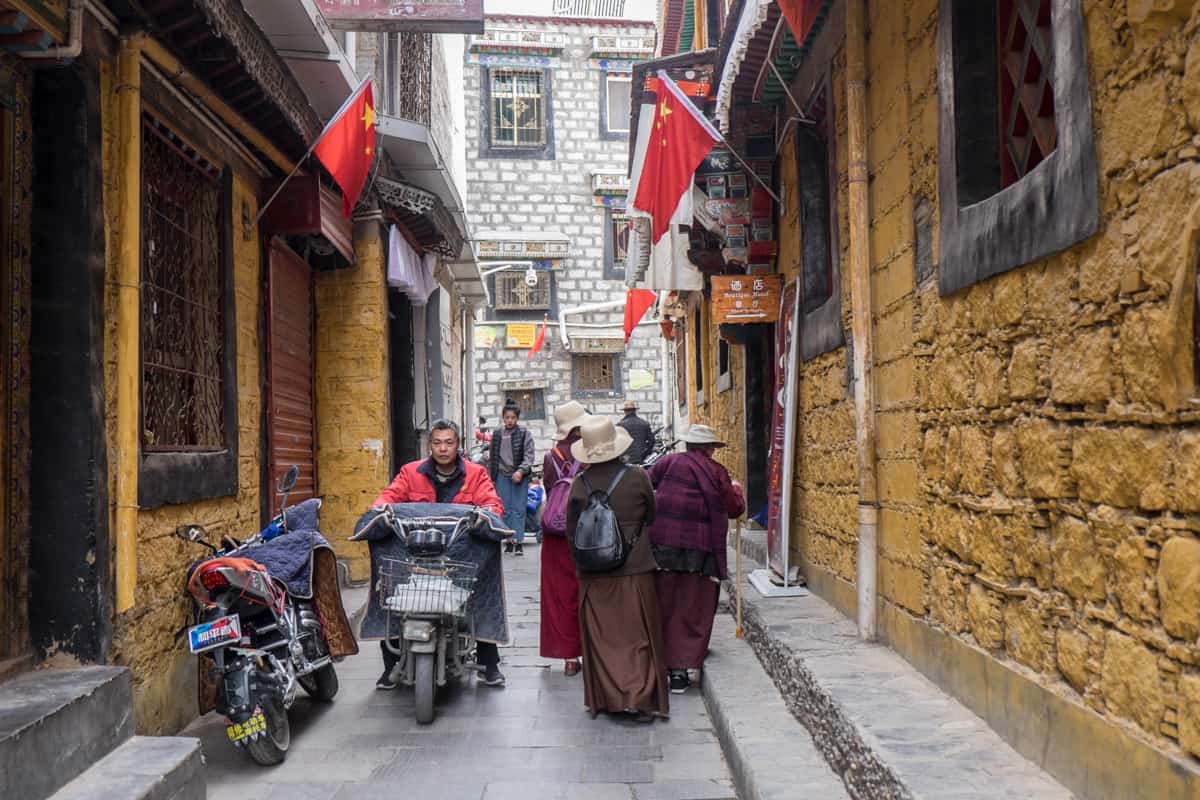 Tibetan women walking down a quiet backstreet with yellow brick walls in Lhasa, Tibet as a man passes them on his motorbike.