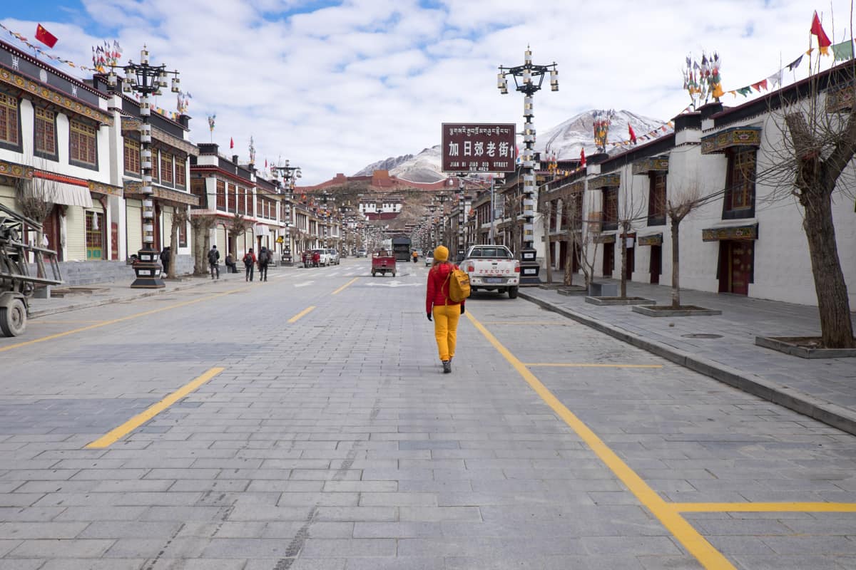 Woman dressed in red and yellow walks down the main road in Gyantse, Tibet which is surrounded by mountains that dominate the view in the background