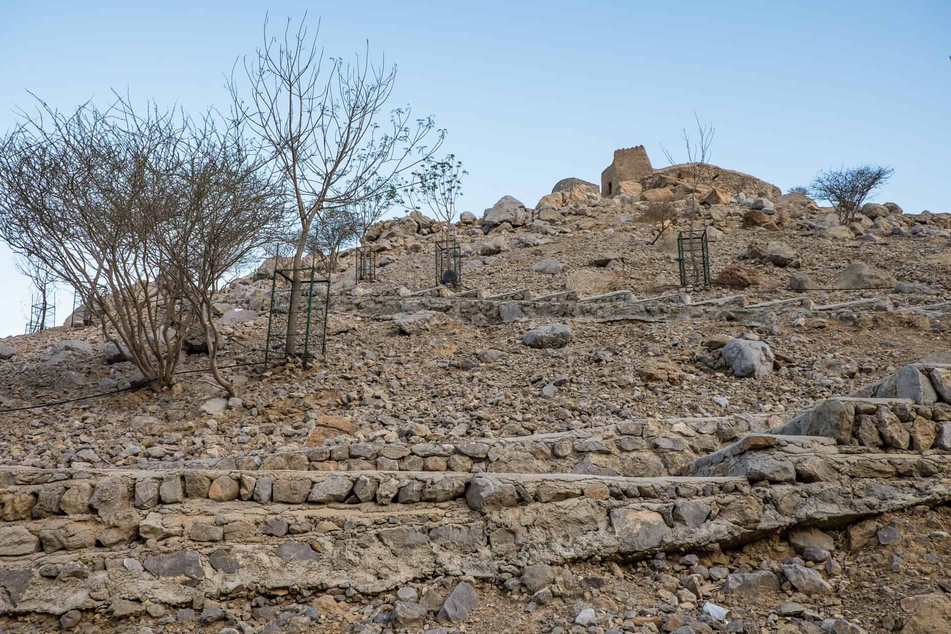 Dry, sandy, rocky zigzag pathway up a mound with a fortification on top in Ras Al Khaimah. 