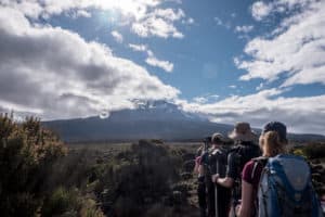 A small trekking group climbing Kilimanjaro moorland with a view of the snow-capped Kibo Peak ahead