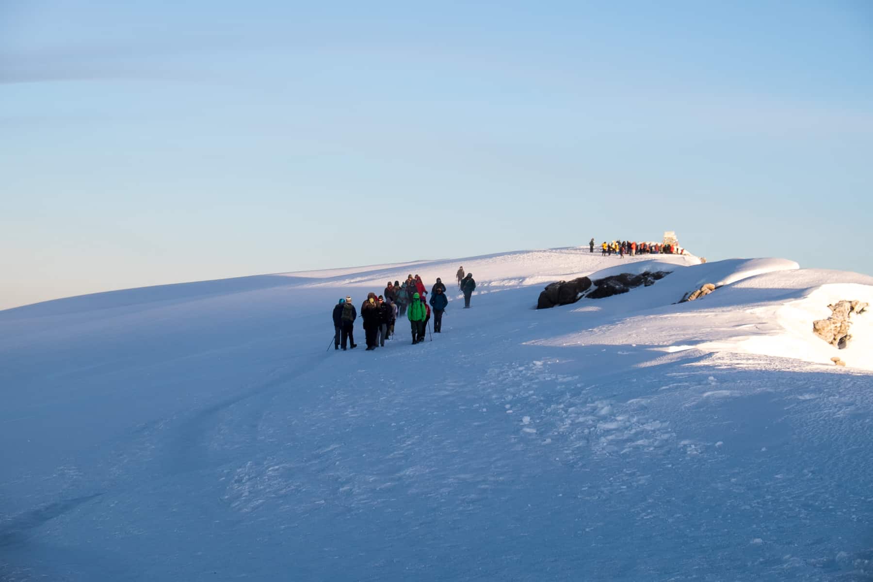 Trekkers on a snow covered mountain peak at The Uhuru Point Summit of Mt. Kilimanjaro.