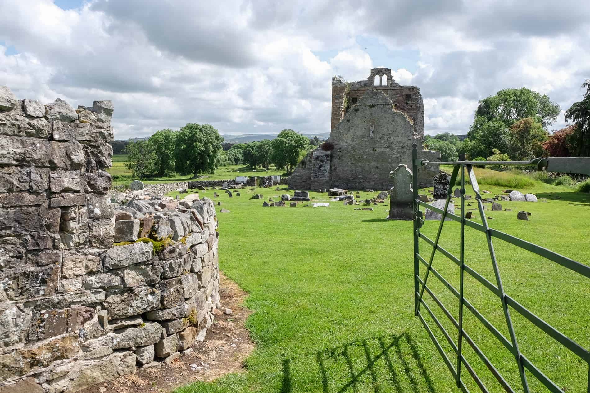 A brick wall and a green metal gate mark the entrance to the ruins of the Jerpoint Park Lost City in Ireland. 