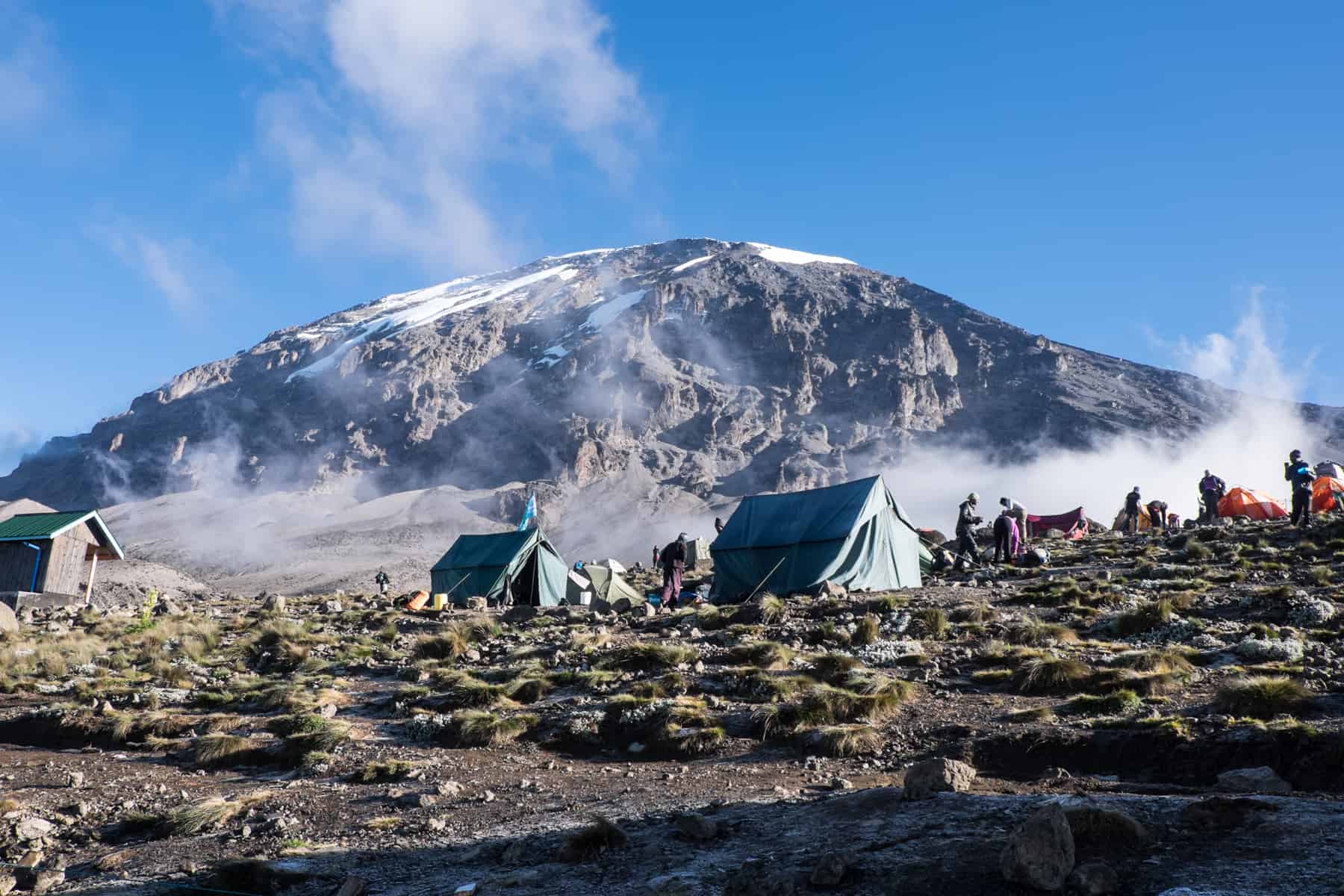 Two large green tents, at a campsite set up at the base of the snow-capped Kilimanjaro mountain. 