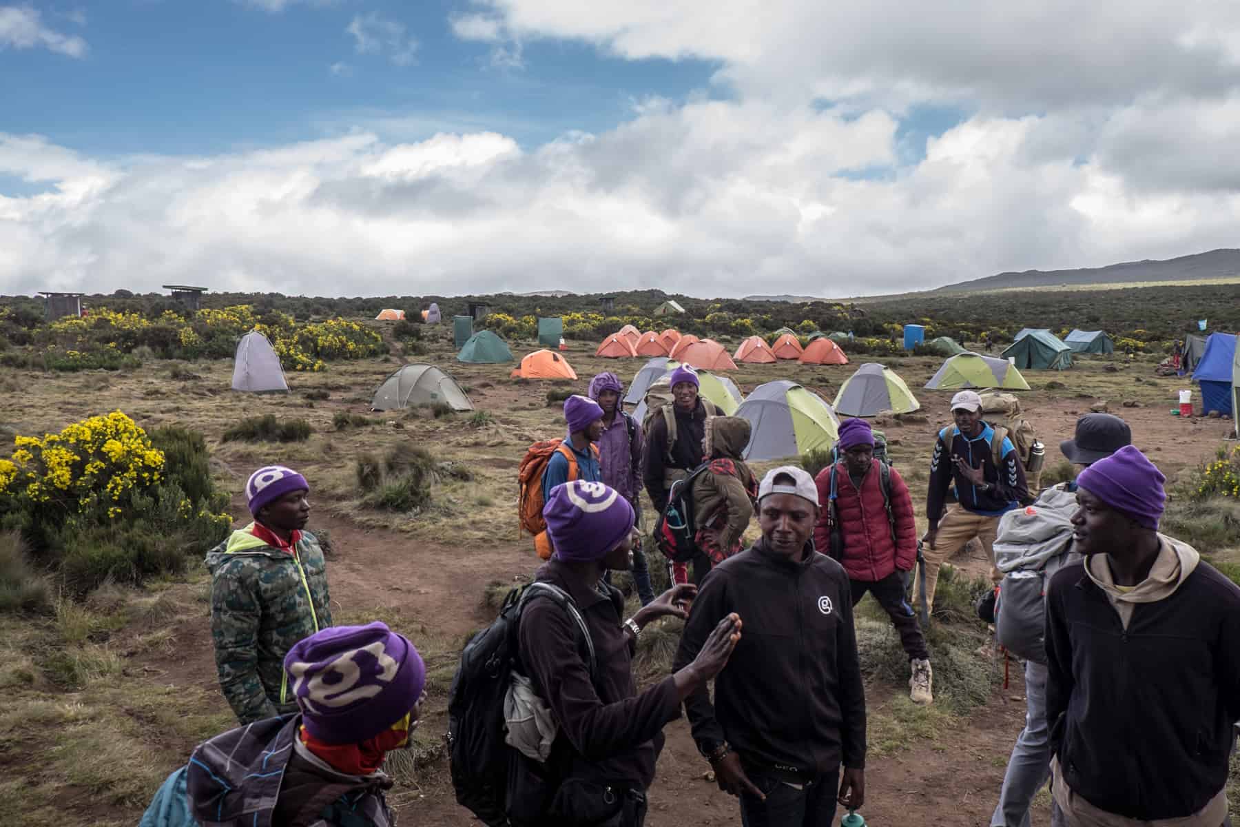 A group of porters in front of a camp on the dry-grassy plains of Mount Kilimanjaro. 
