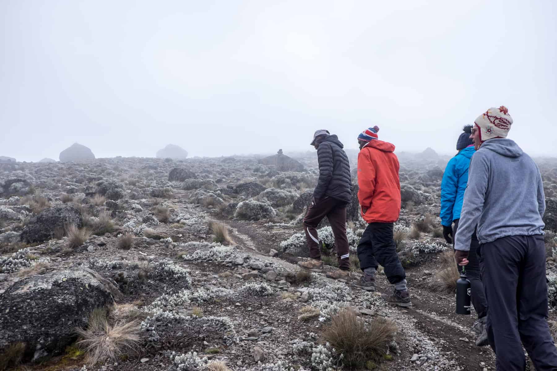 Four trekkers wearing black, red and blue hike up a rocky scree covered in mist on Kilimanjaro.