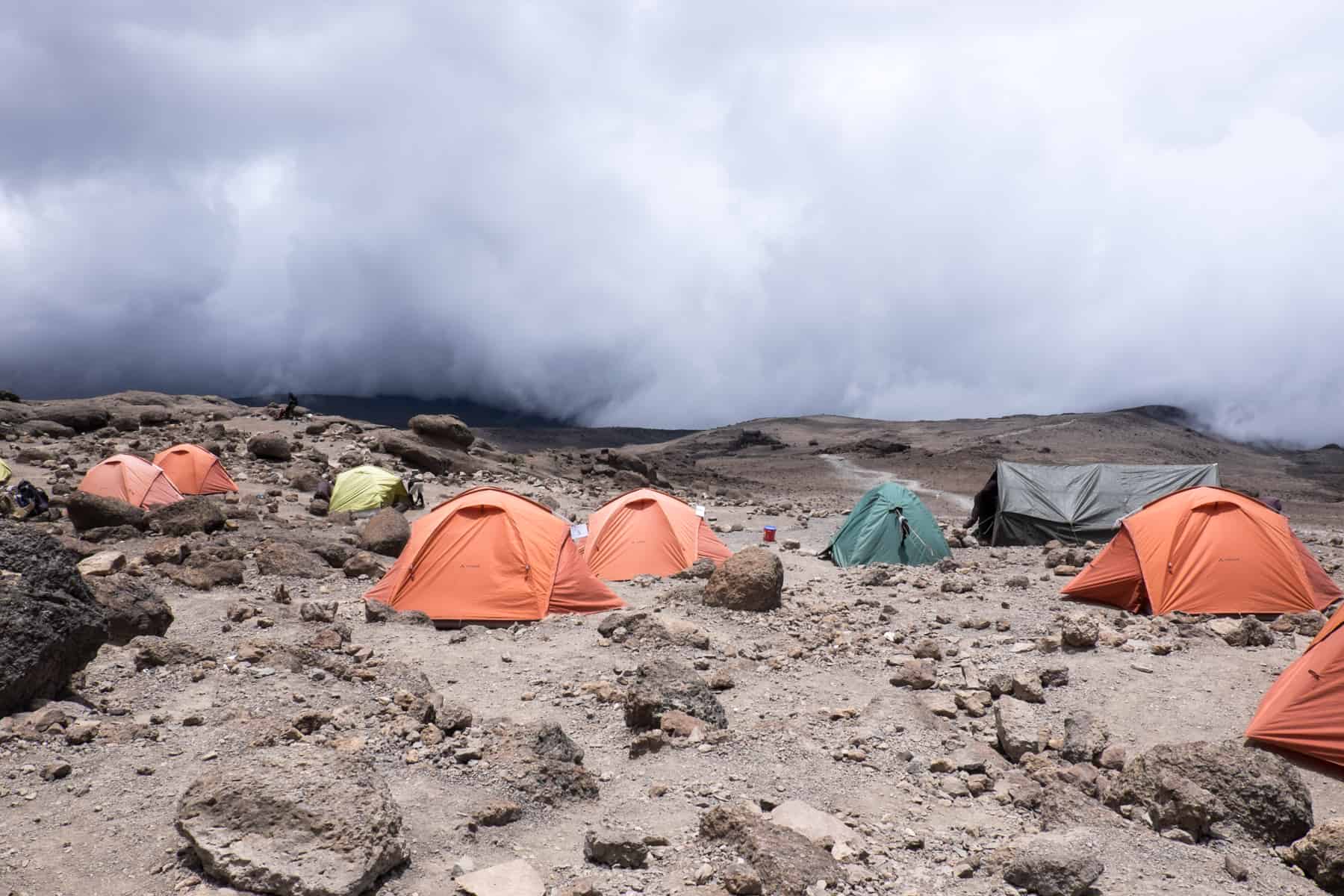 A campsite of orange and green tents on rocky ground on Mount Kilimanjaro.