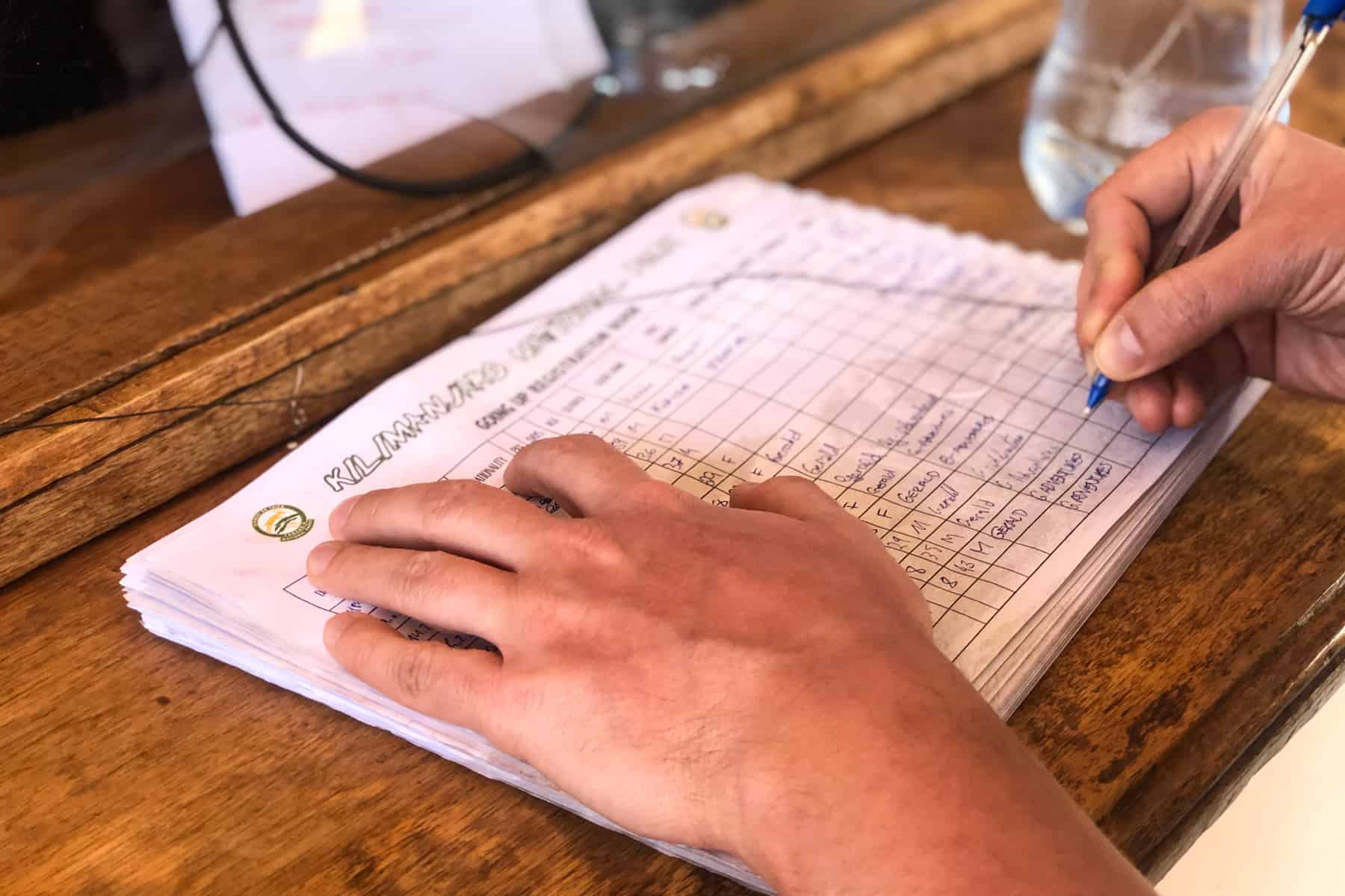 A man writes his details on a white lined notebook, checking into a camp on Kilimanjaro