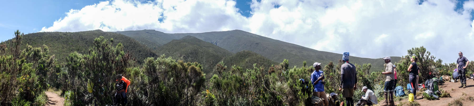 A group of trekkers stand upon a high hill looking out over the Kilimanjaro valley and the 'Elephants Back' ridge