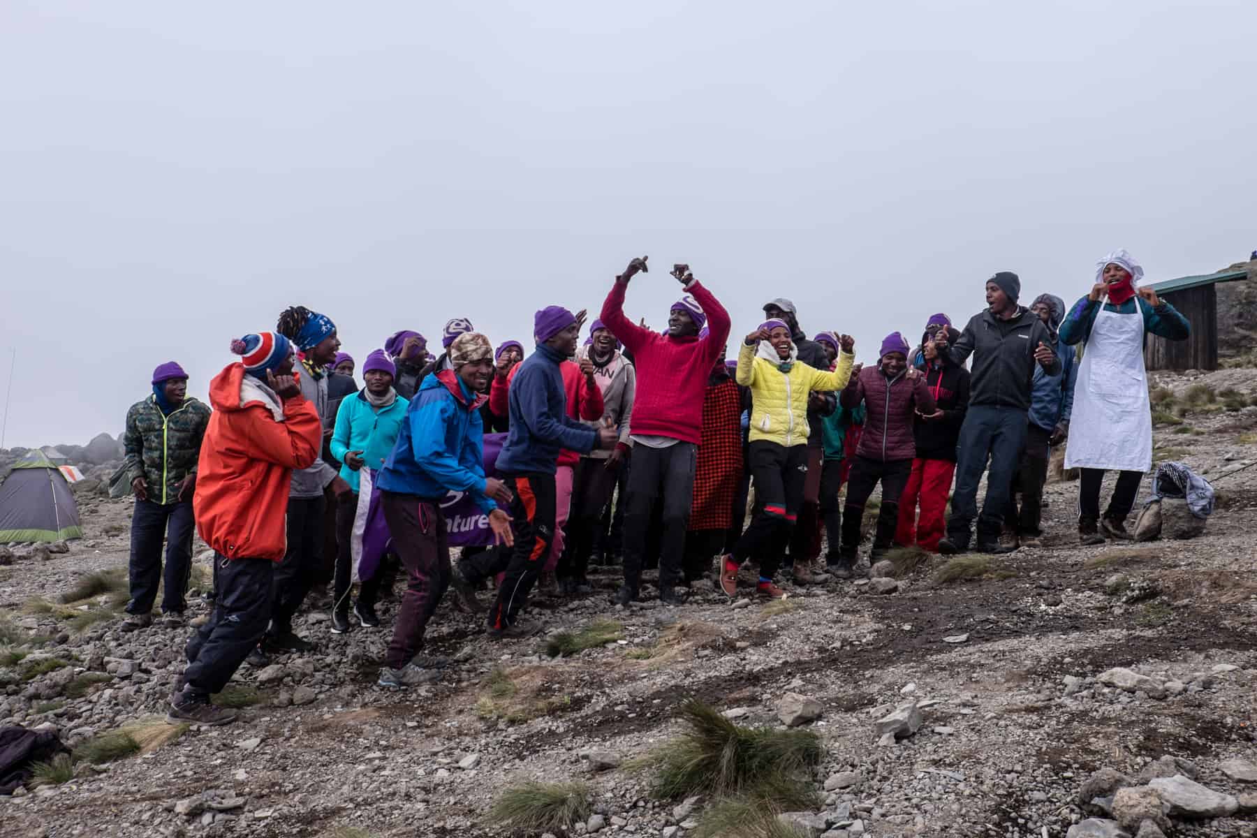 A group of 30 Kilimanjaro porters and guides sing and dance on a mountain slope covered in mist