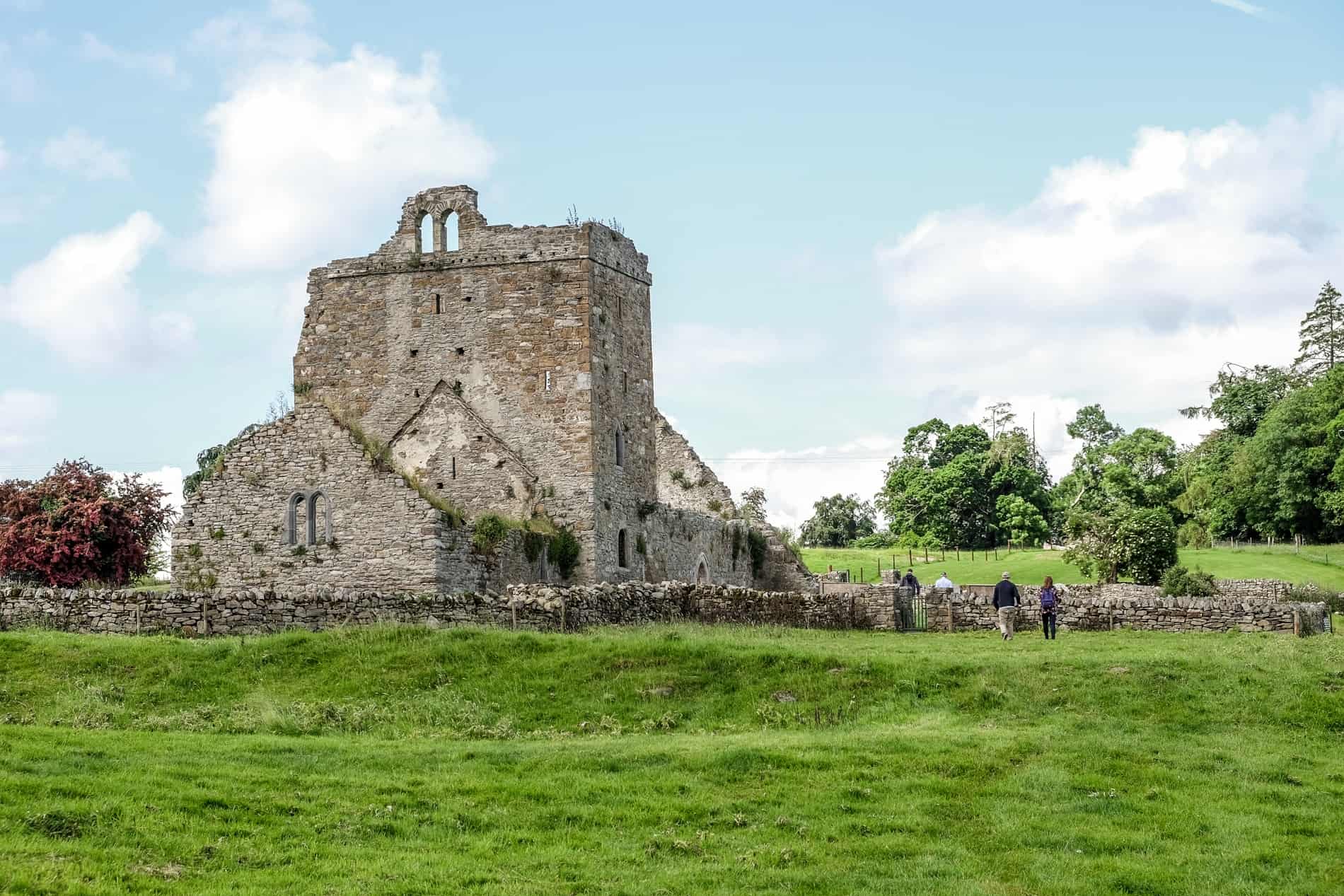 People looking at the stone ruin walls standing on the green Irish farmland of Jerpoint Park in Kilkenny. 