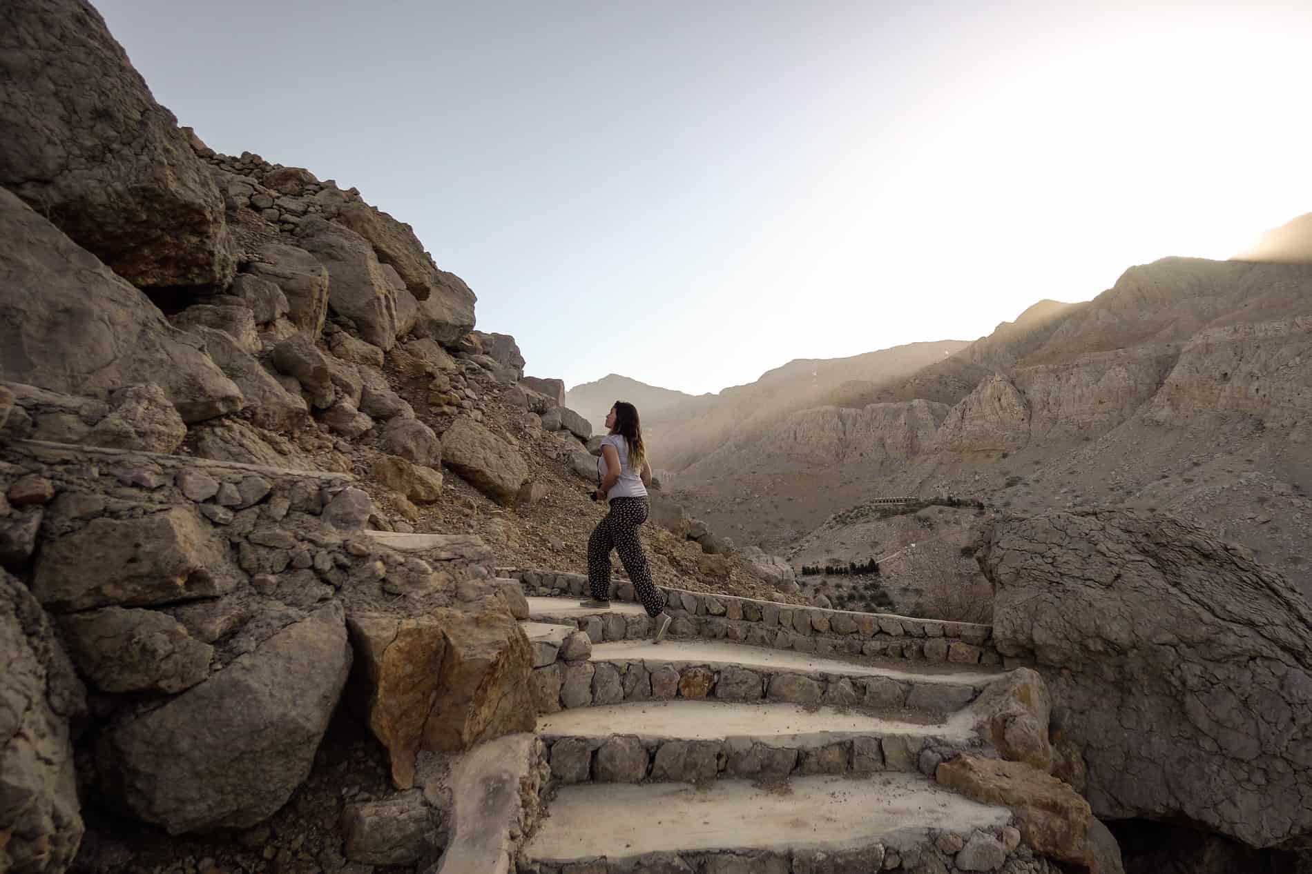 A woman walks up the stone slab stairs on a rocky hill in Ras Al Khaimah. 