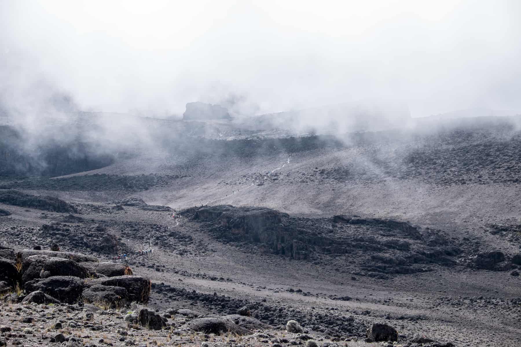The black volcanic valley walls of Mount Kilimanjaro, speckled with the tiny colour of trekkers hiking up the steep white-worn path