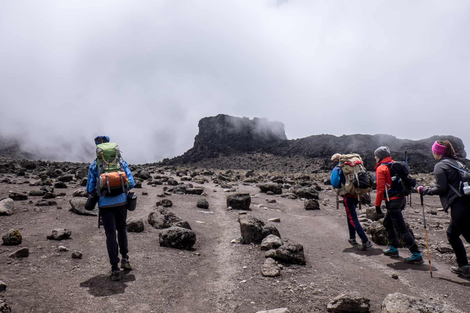 A Kilimanjaro guide on the left and three trekkers on the right pull themselves through the thin air towards the rectangular rock known as the Lava Tower