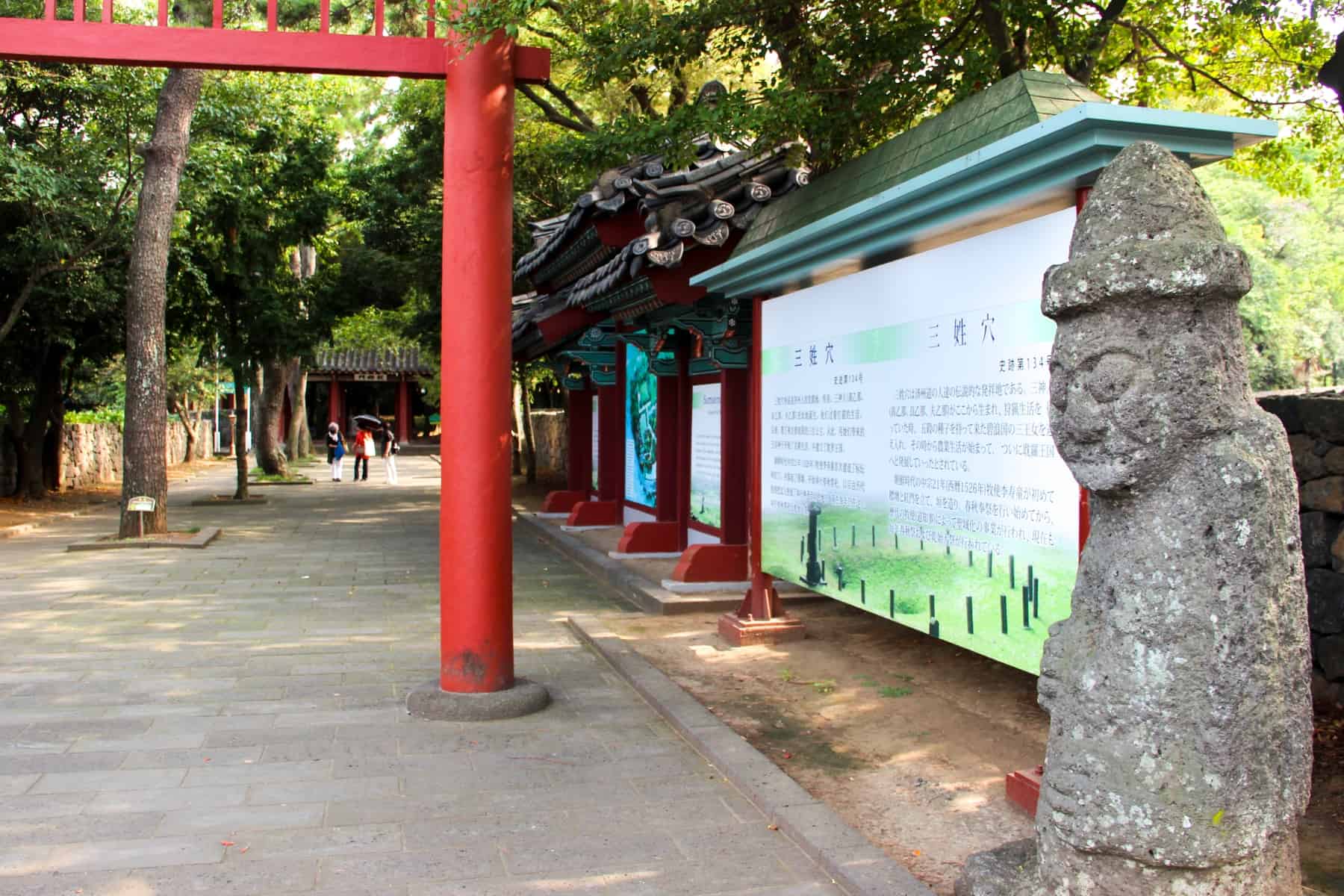 A grey stone statue on Jeju Island is a protection god, known as Dol hareubang. This one stands outside a temple marked by a red gate 