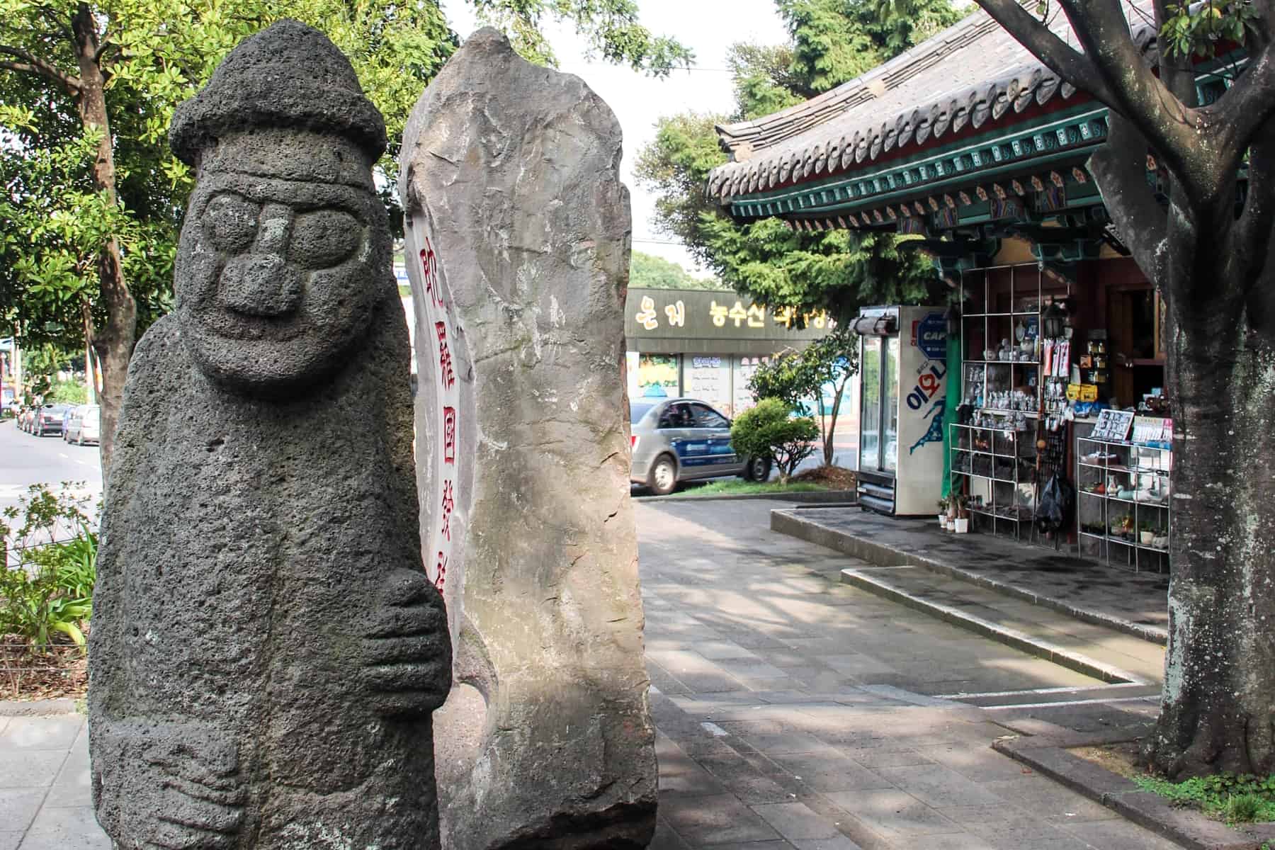 the male looking, bulging eyed Jeju Island Dol hareubang Stone Statues. Este fica do lado de fora de uma loja, e diz-se que oferece protecção.