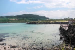 A white sand beach overed by aqua blue sea water, backed by high green hills - a scene of nature on Jeju Island, Korea